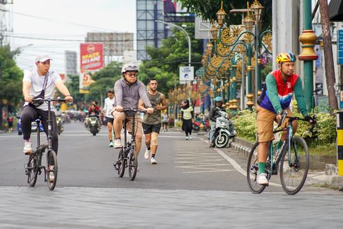 Free City street scene capturing cyclists and a jogger in a vibrant morning atmosphere. Stock Photo