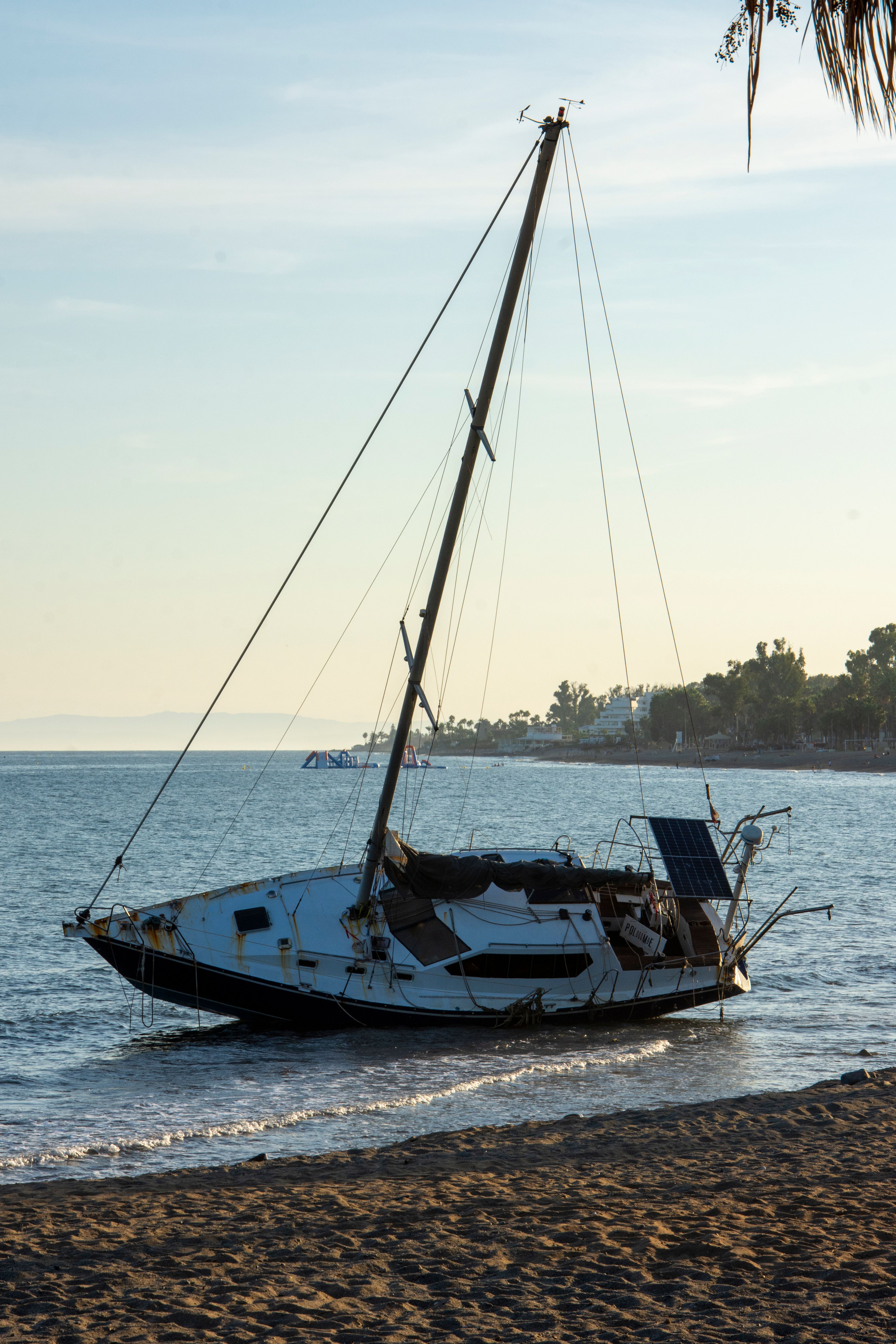 A deserted sailboat rests on the sandy shores of Marbella during sunset.