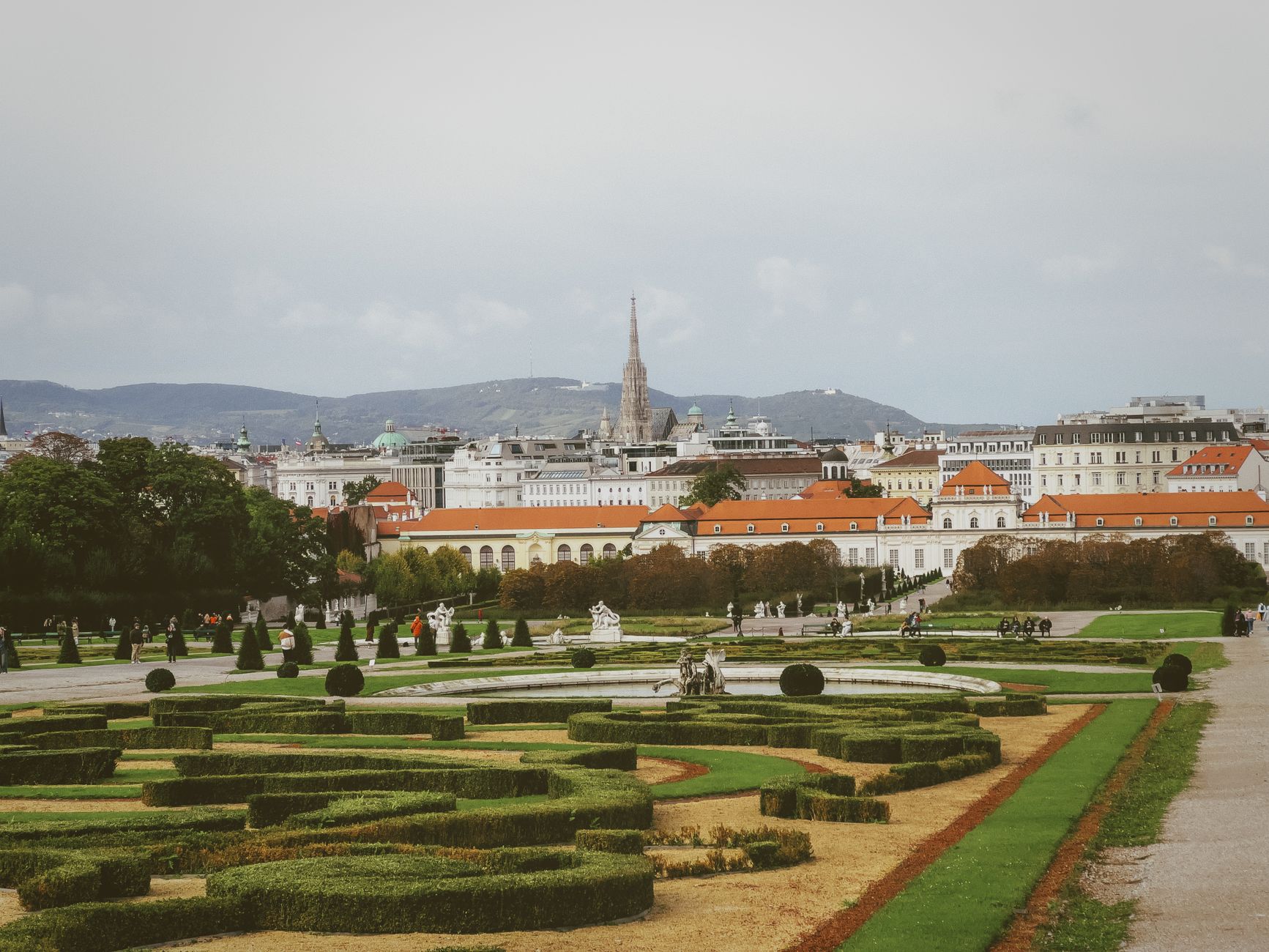A scenic view of Vienna's Belvedere Gardens and city skyline with mountains in the background.