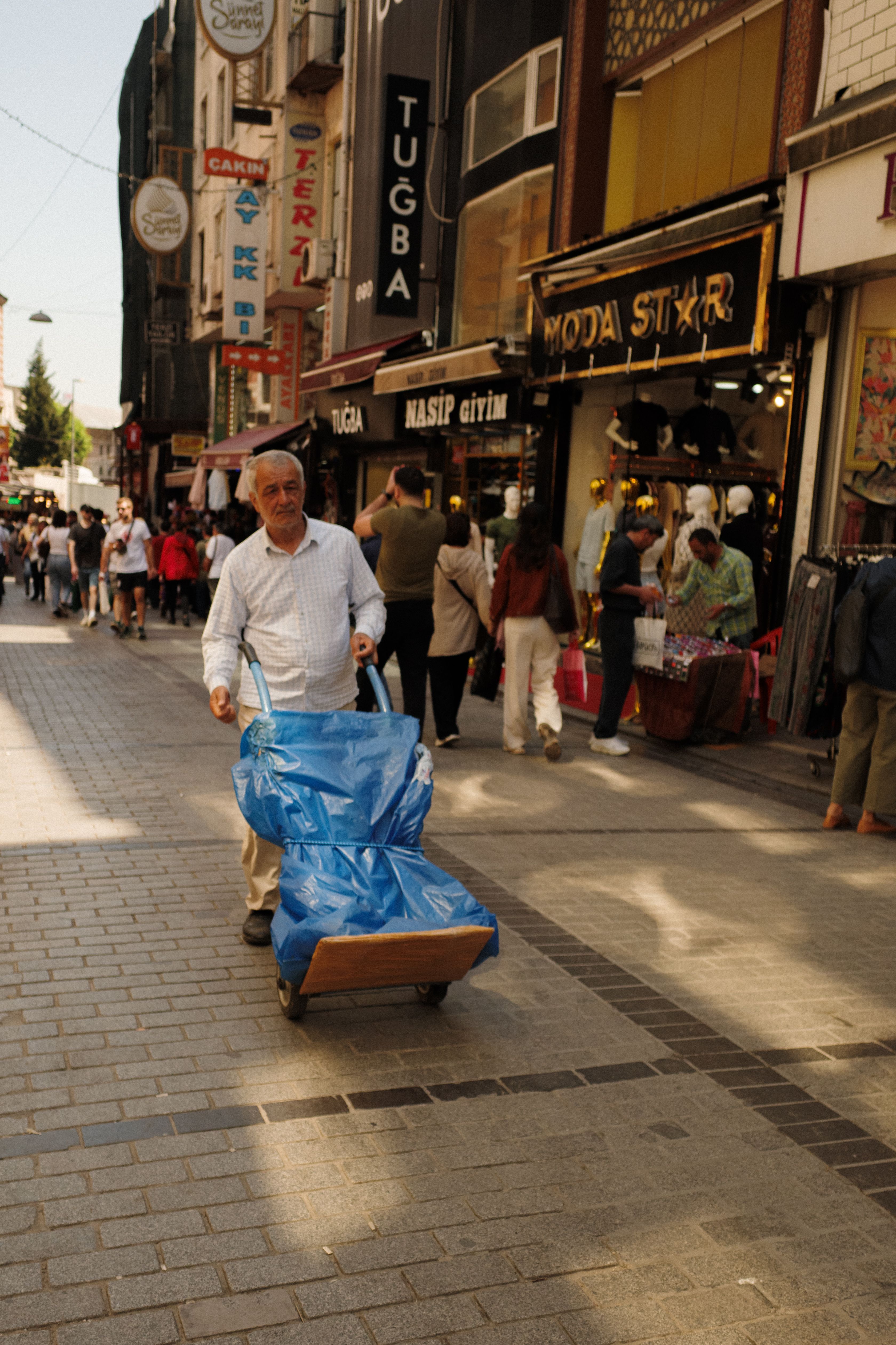 A lively street scene in Istanbul featuring a man wheeling a cart, surrounded by shoppers.