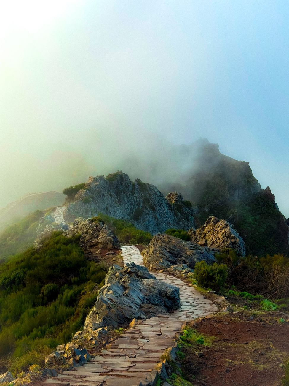 A scenic mountain pathway surrounded by fog, offering a serene hiking experience.