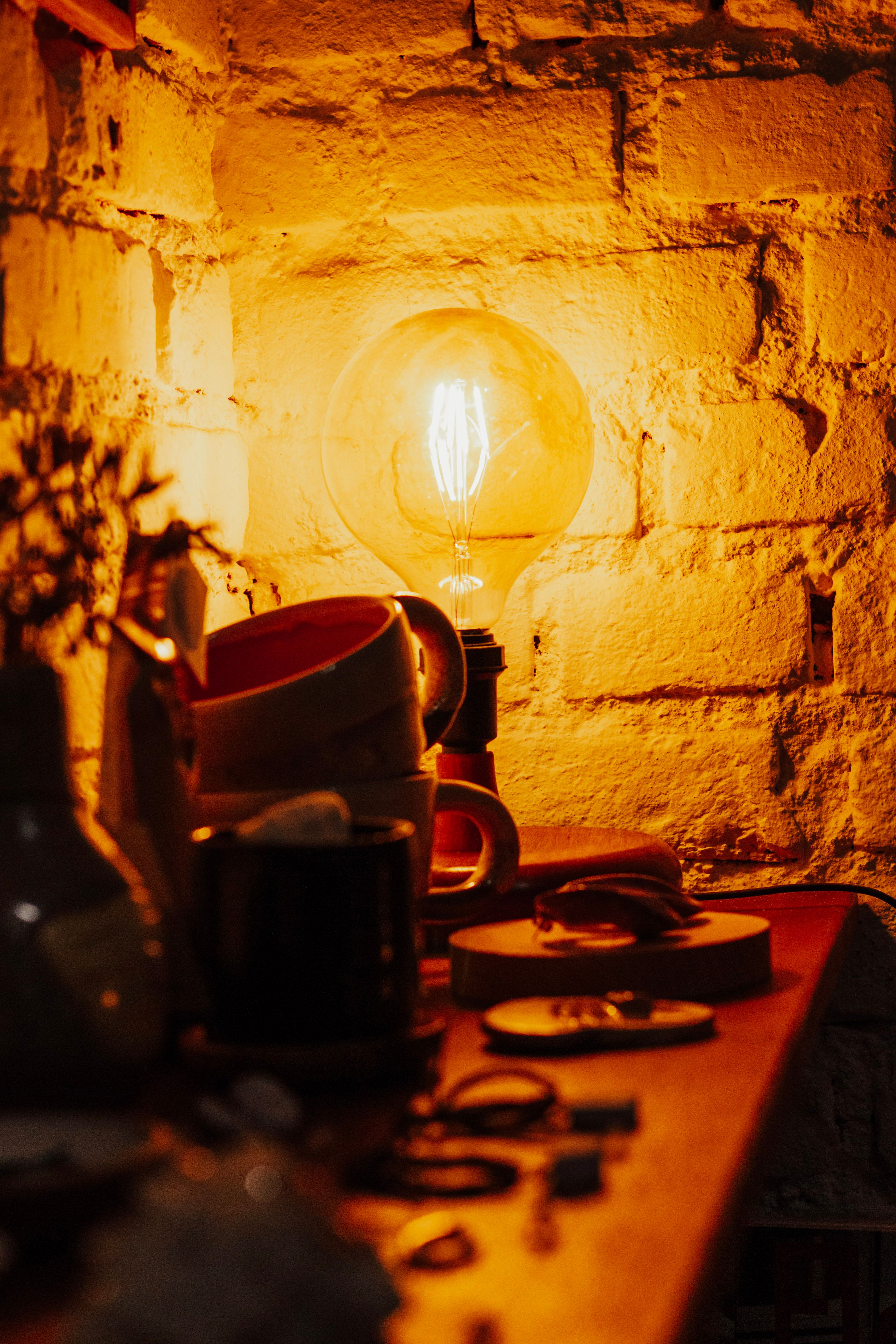 Warm glowing light bulb illuminating a rustic brick wall with ceramic decor.
