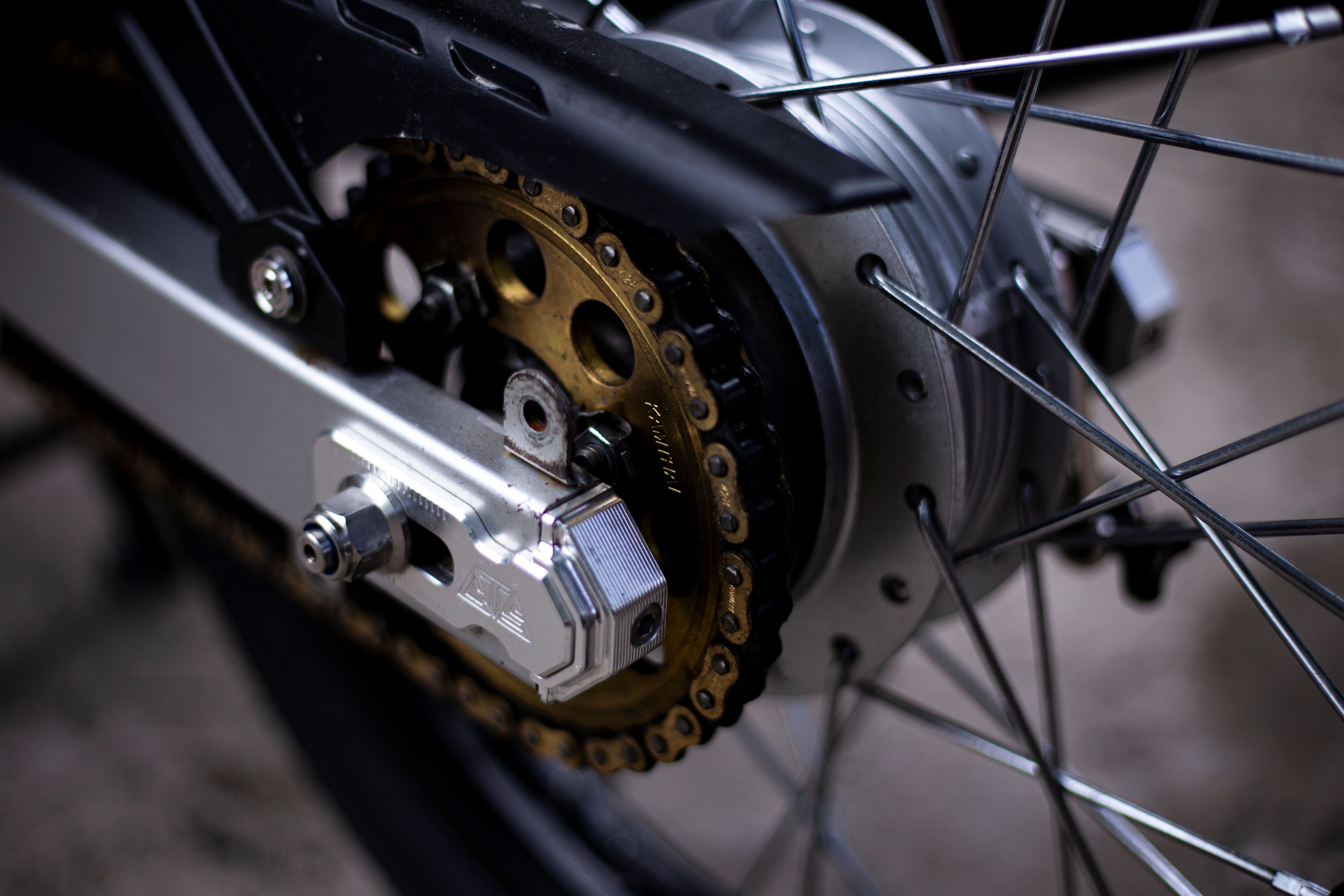 Gratis Detaljeret visning af en motorcykels baghjul, der viser gear og kæde i fokus, taget udendørs. Lagerfoto