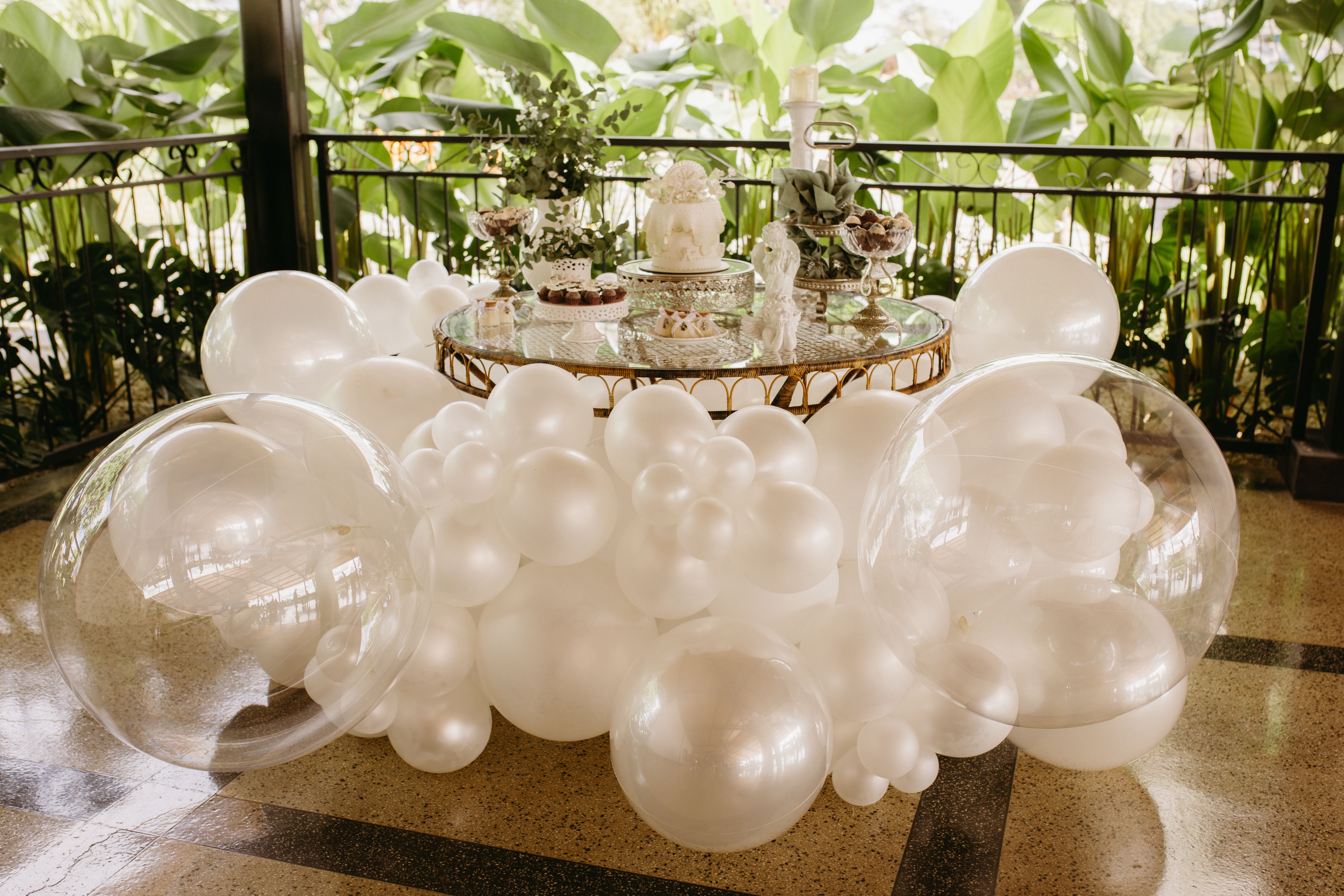 Beautiful wedding table setup with white balloons and decorative cakes surrounded by greenery.