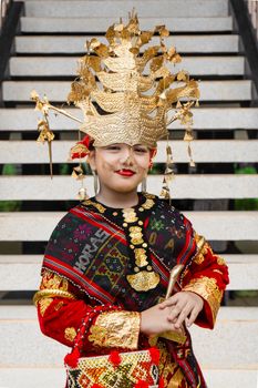 Child in vibrant traditional costume and gold headdress poses on stairs, showcasing cultural heritage. - Fotografer Sidoarjo