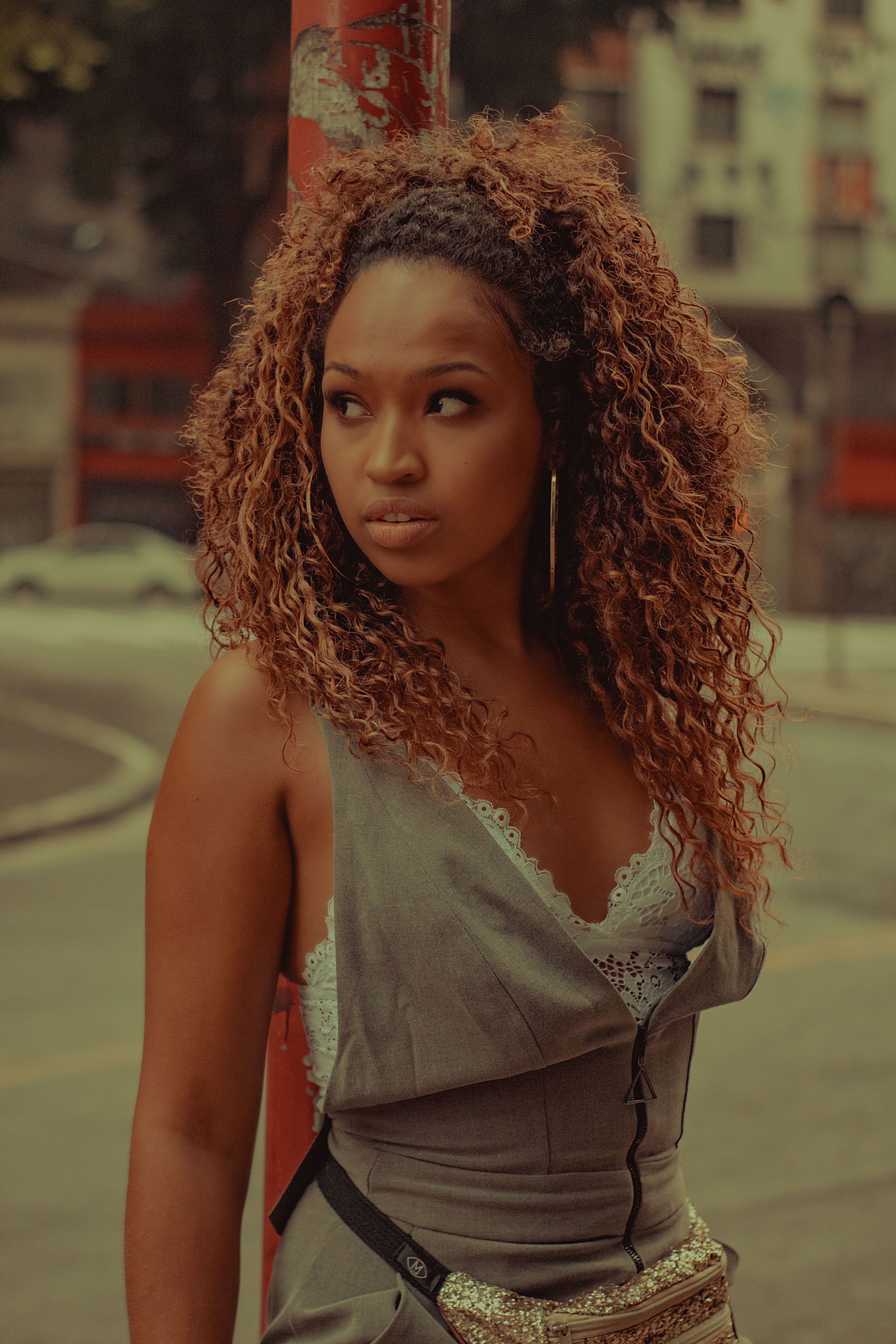 A fashionable woman with curly hair poses confidently outdoors on a city street.