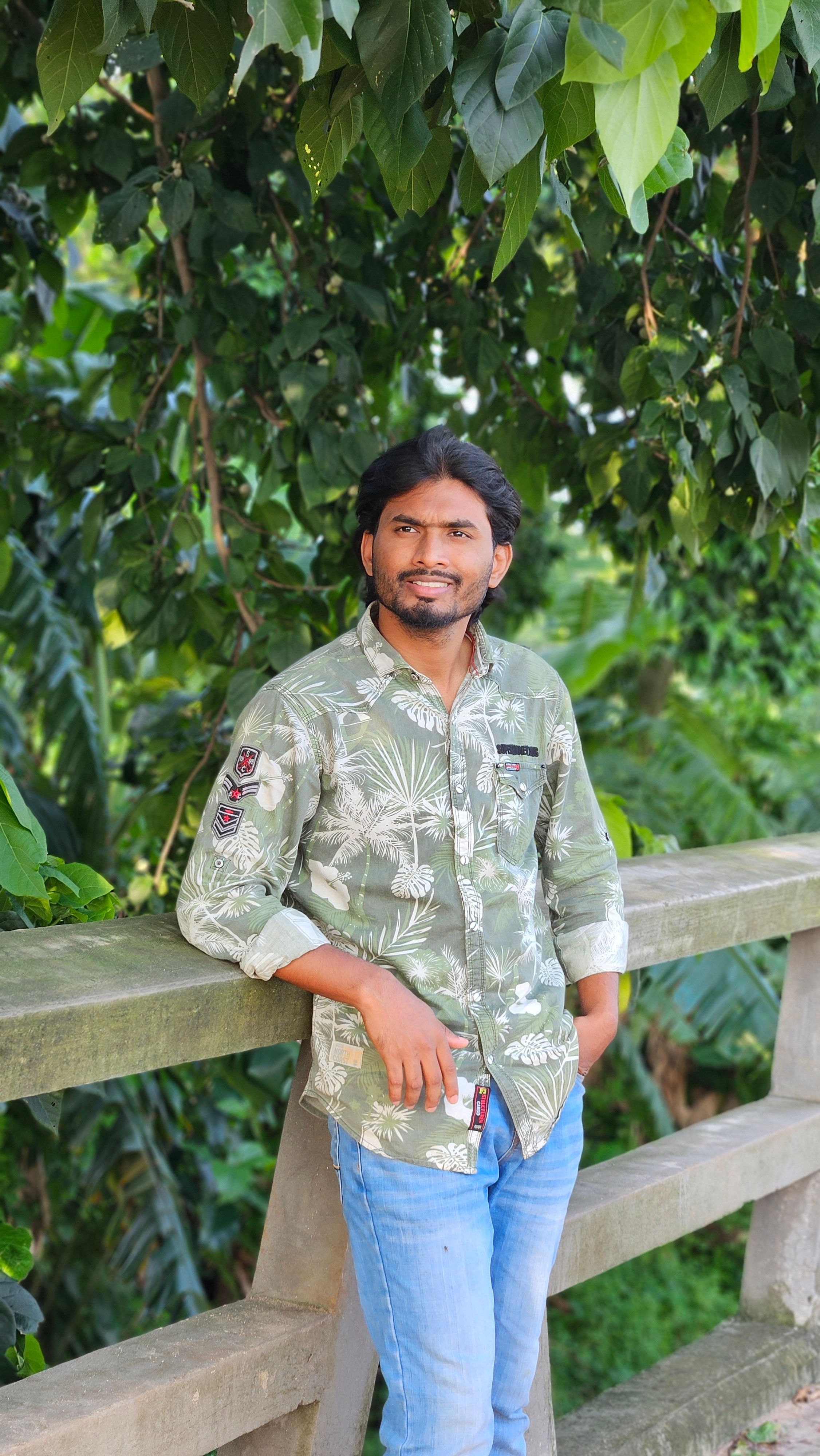 A man in casual attire standing on a wooden bridge amid lush greenery.