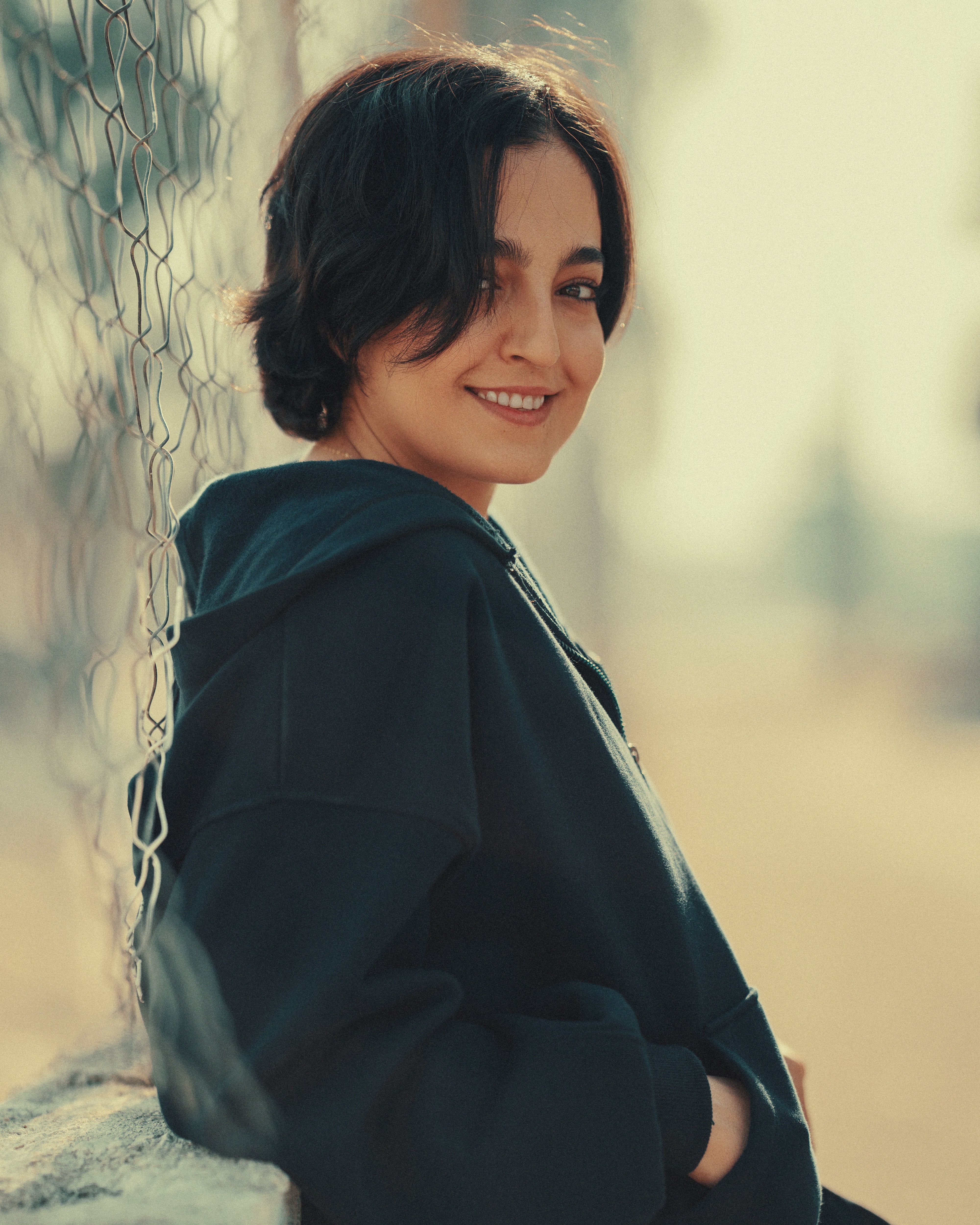 A moody, candid portrait of a young woman smiling outdoors in soft natural light.