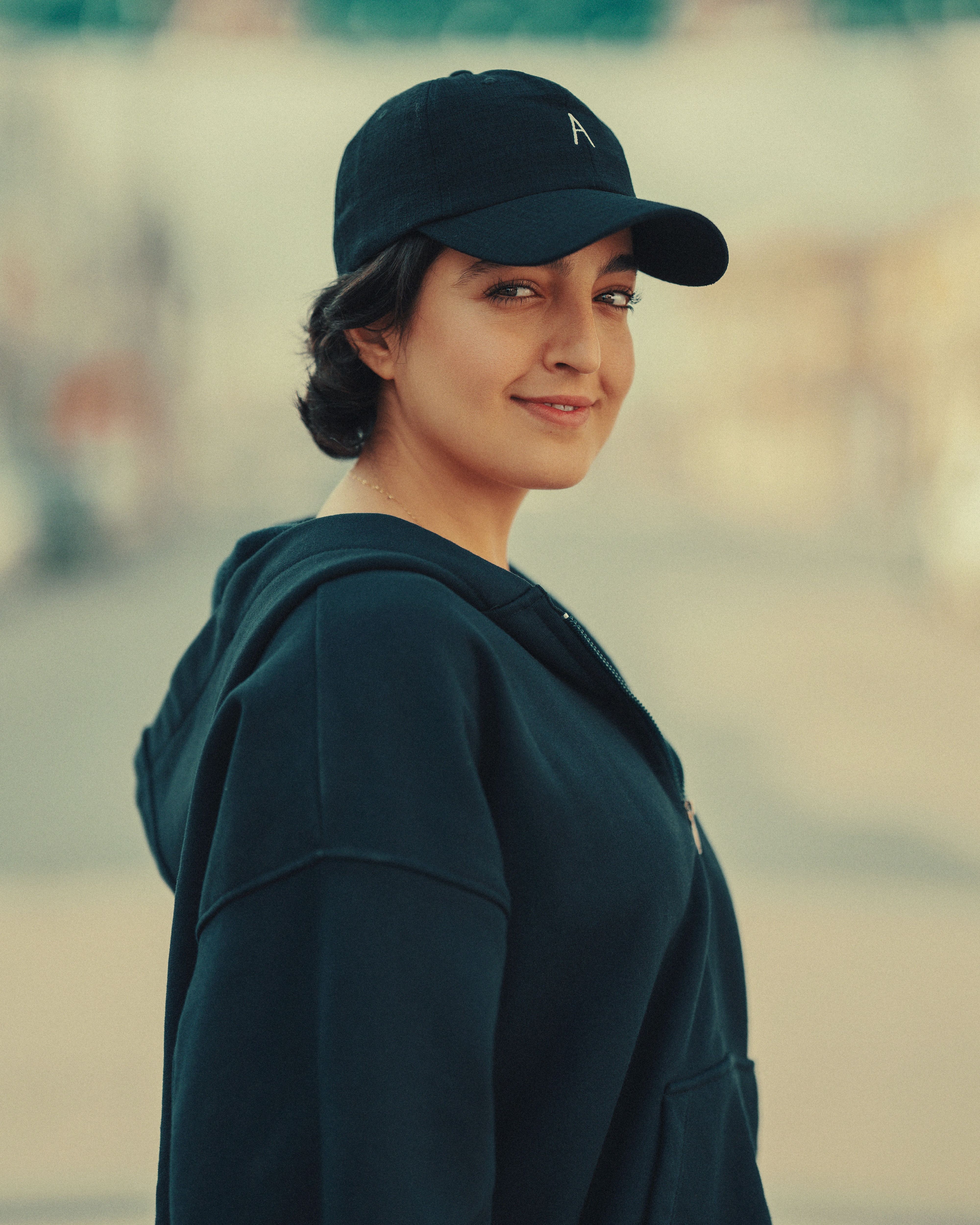 Candid portrait of a young woman in a black hoodie and cap, softly lit outdoors.