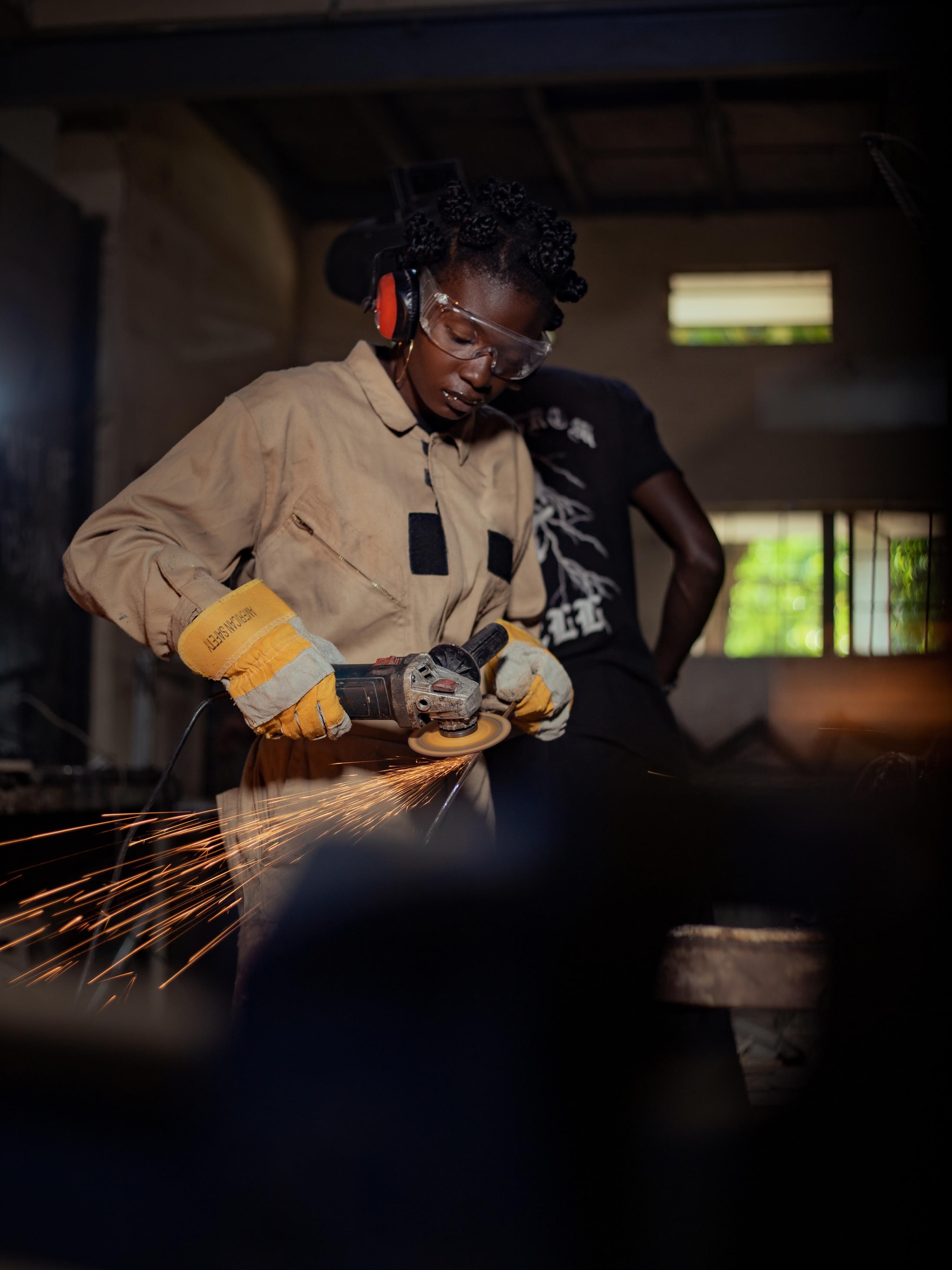 Portrait of a female welder in protective gear grinding metal in a workshop.