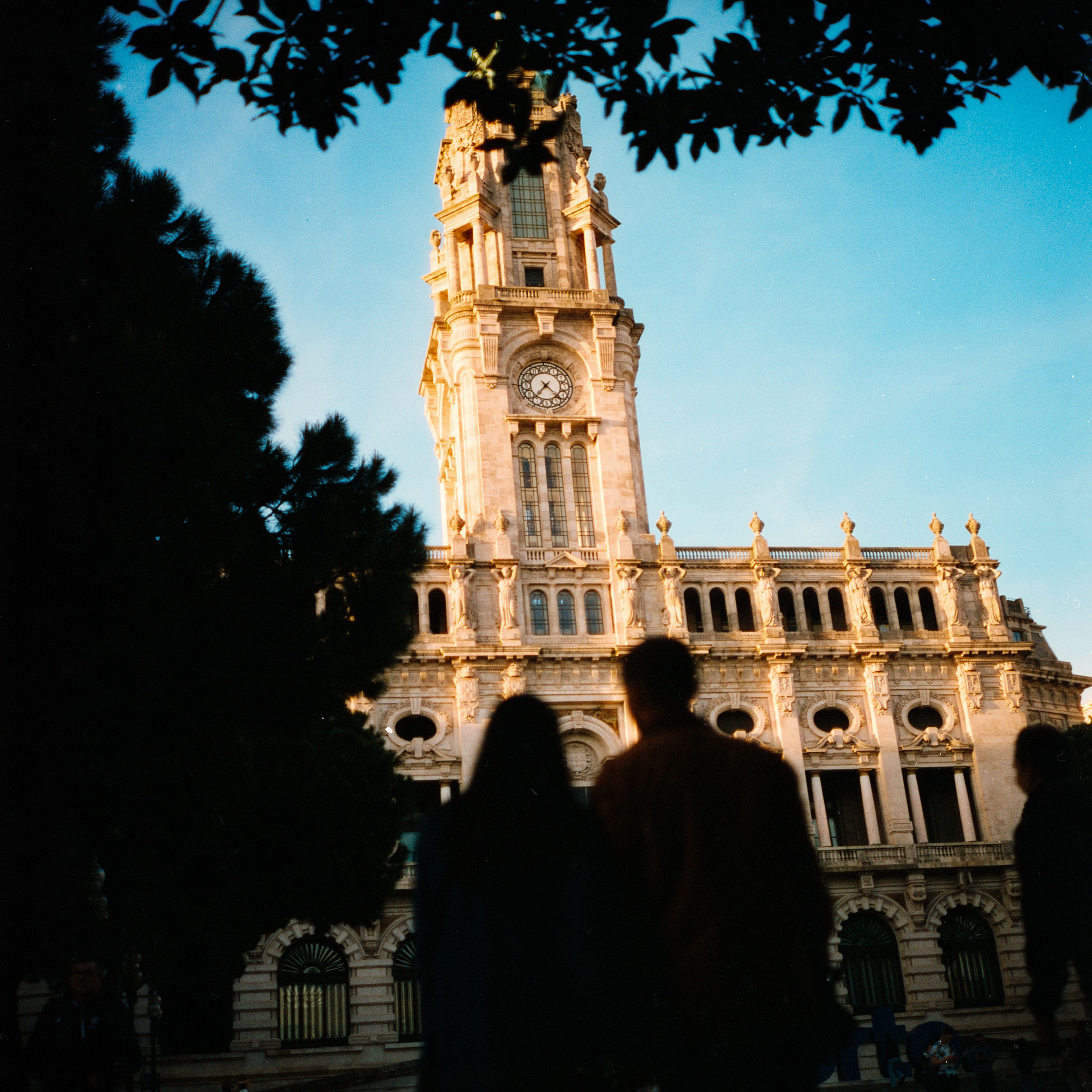 Silhouetted couple gazing at Porto City Hall under a clear blue sky.