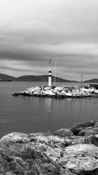 A scenic black and white photograph of a solitary lighthouse on a rocky coast under dramatic clouds.