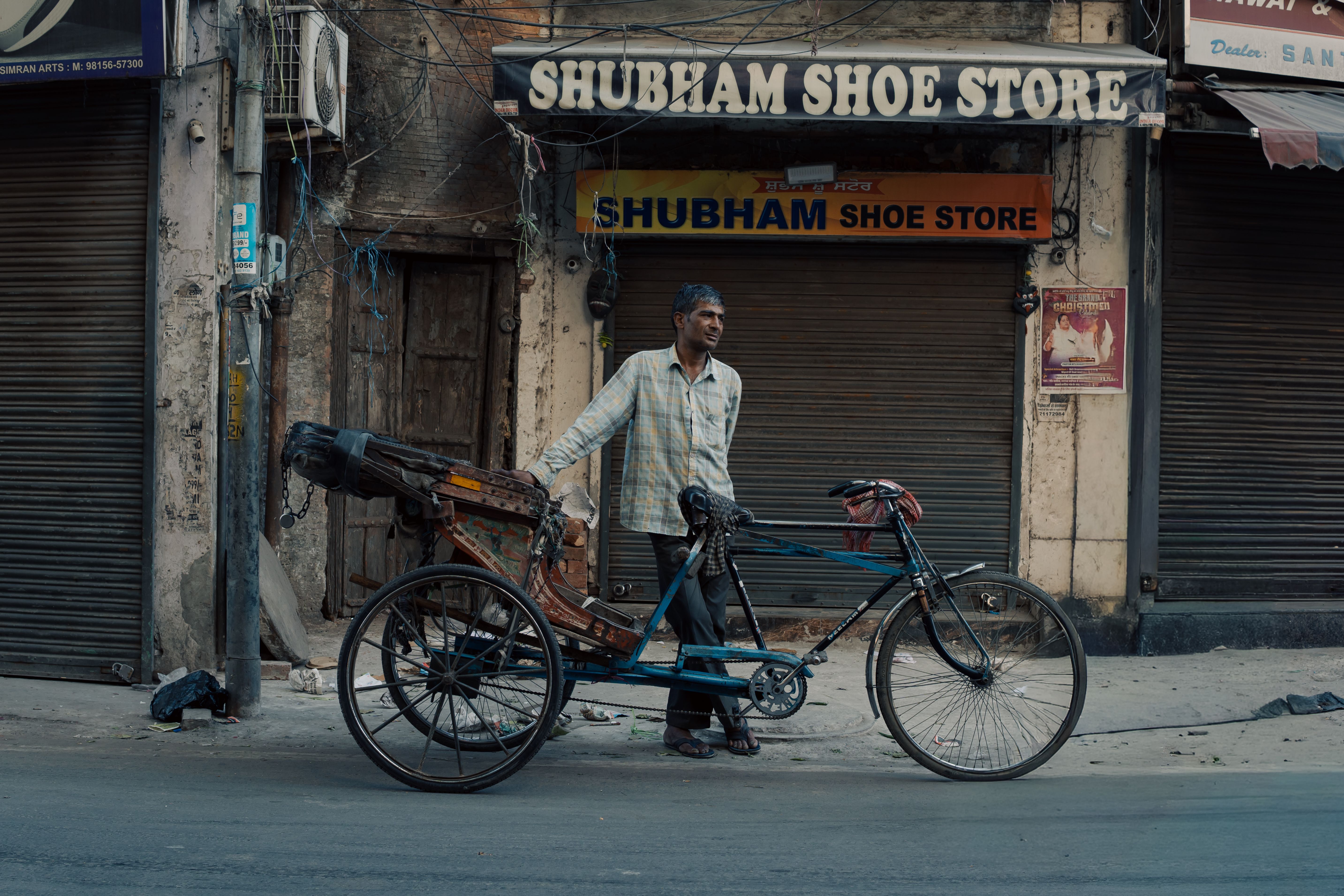 A street vendor with a rickshaw stands outside a closed shoe store in Ludhiana, depicting daily life.