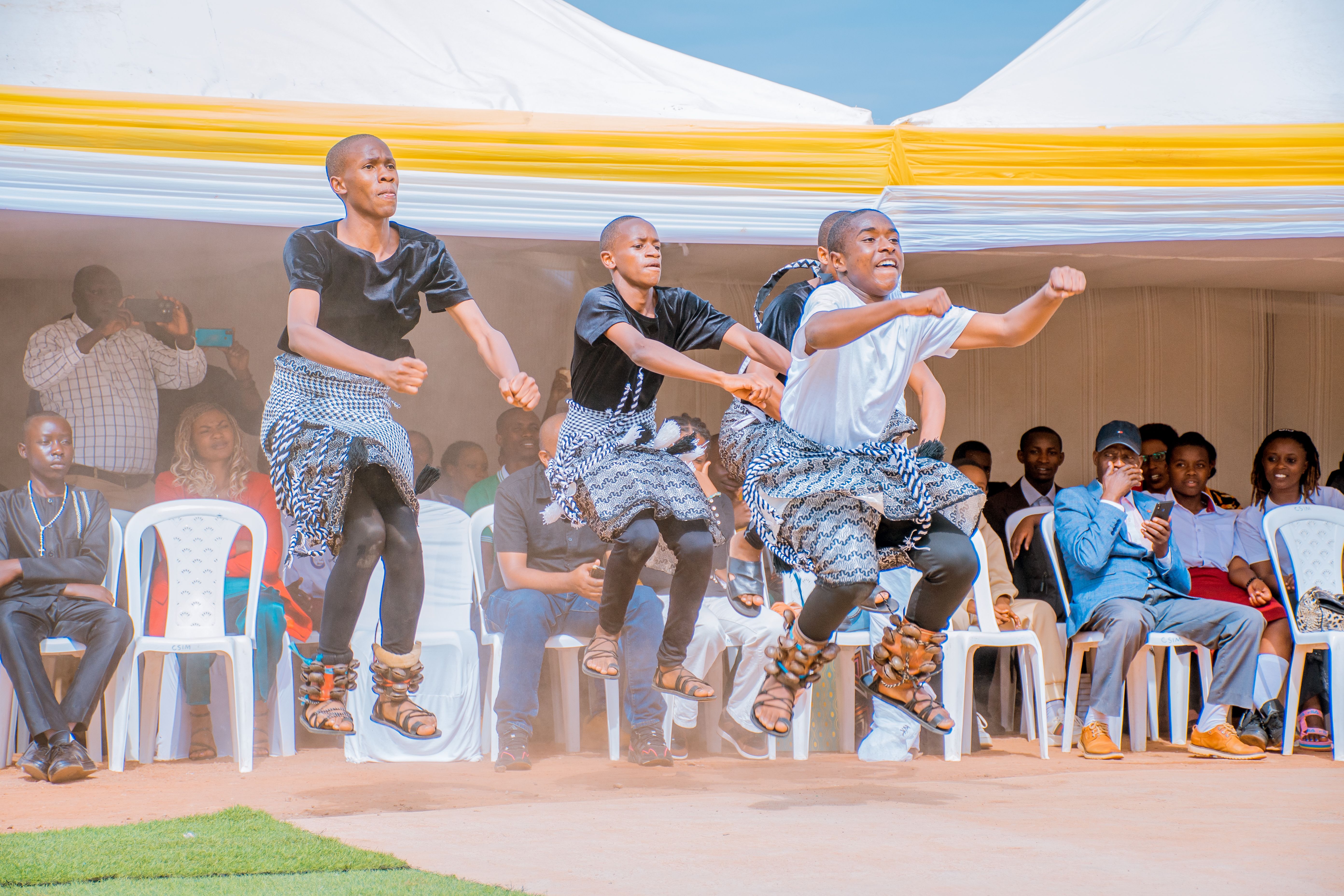 Group of dancers performing traditional dance in cultural attire at outdoor event with audience.