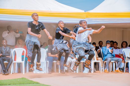 Group of dancers performing traditional dance in cultural attire at outdoor event with audience.