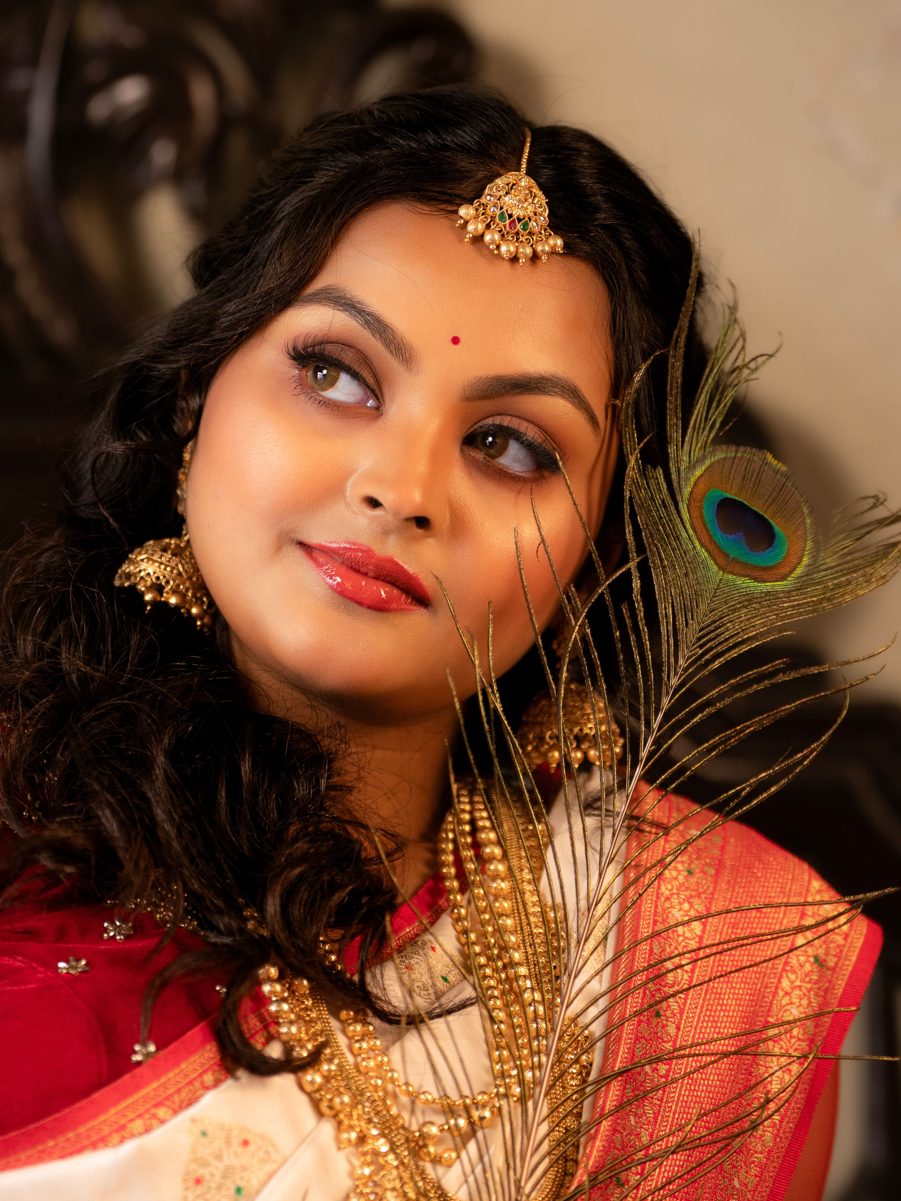 Portrait of a beautiful Indian woman wearing traditional attire and jewelry, holding a peacock feather.