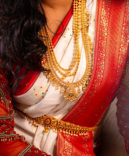 Free Close-up of a red and white saree adorned with intricate gold jewelry, highlighting traditional Indian fashion. Stock Photo