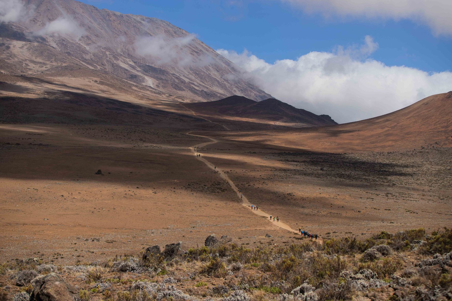 Scenic view of a trekking path on Mount Kilimanjaro, highlighting the arid landscape and distant climbers.