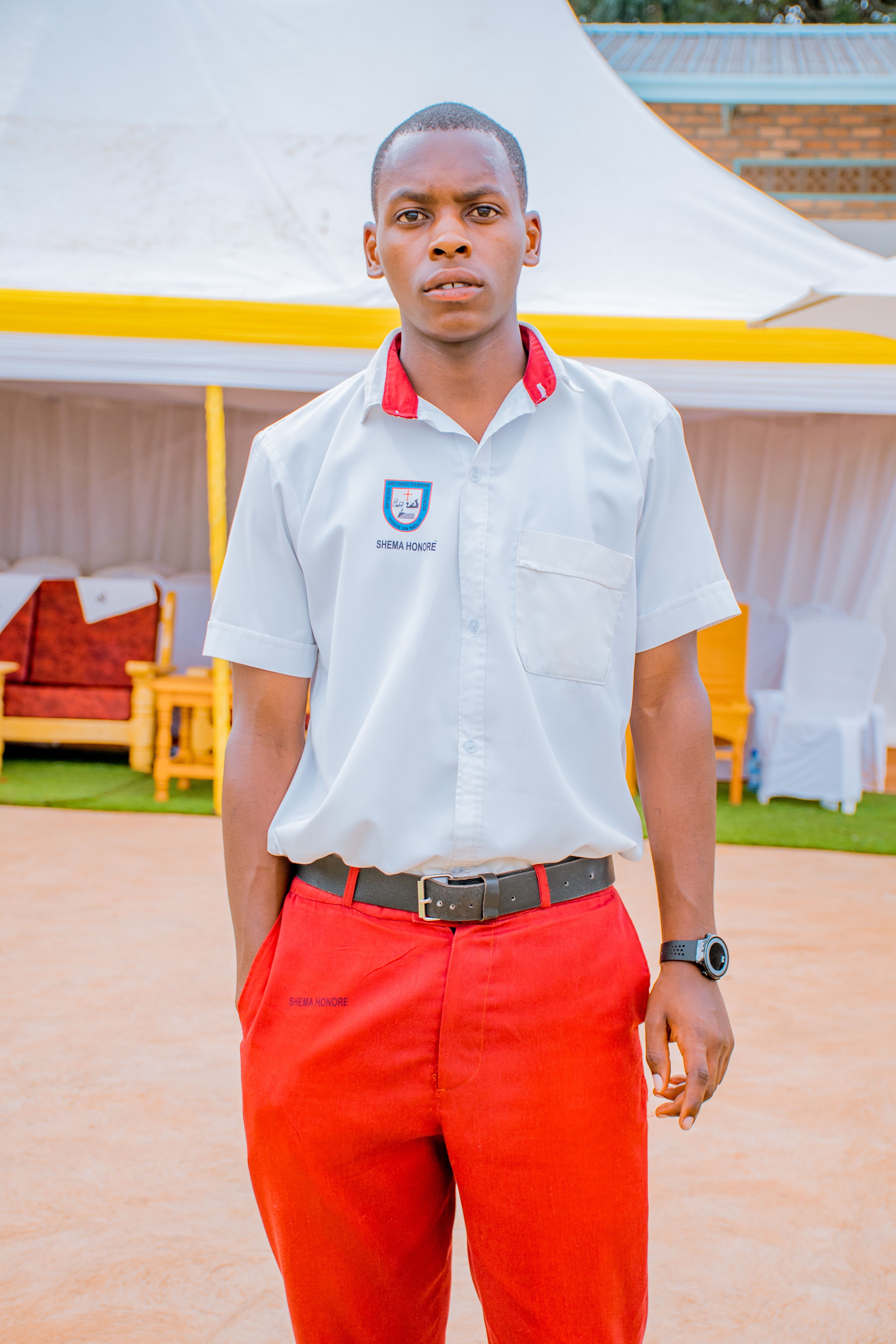 A young man wearing a school uniform stands confidently in an outdoor setting near a tent.