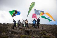 A group of hikers celebrates reaching the summit of Mount Kilimanjaro with various national flags.