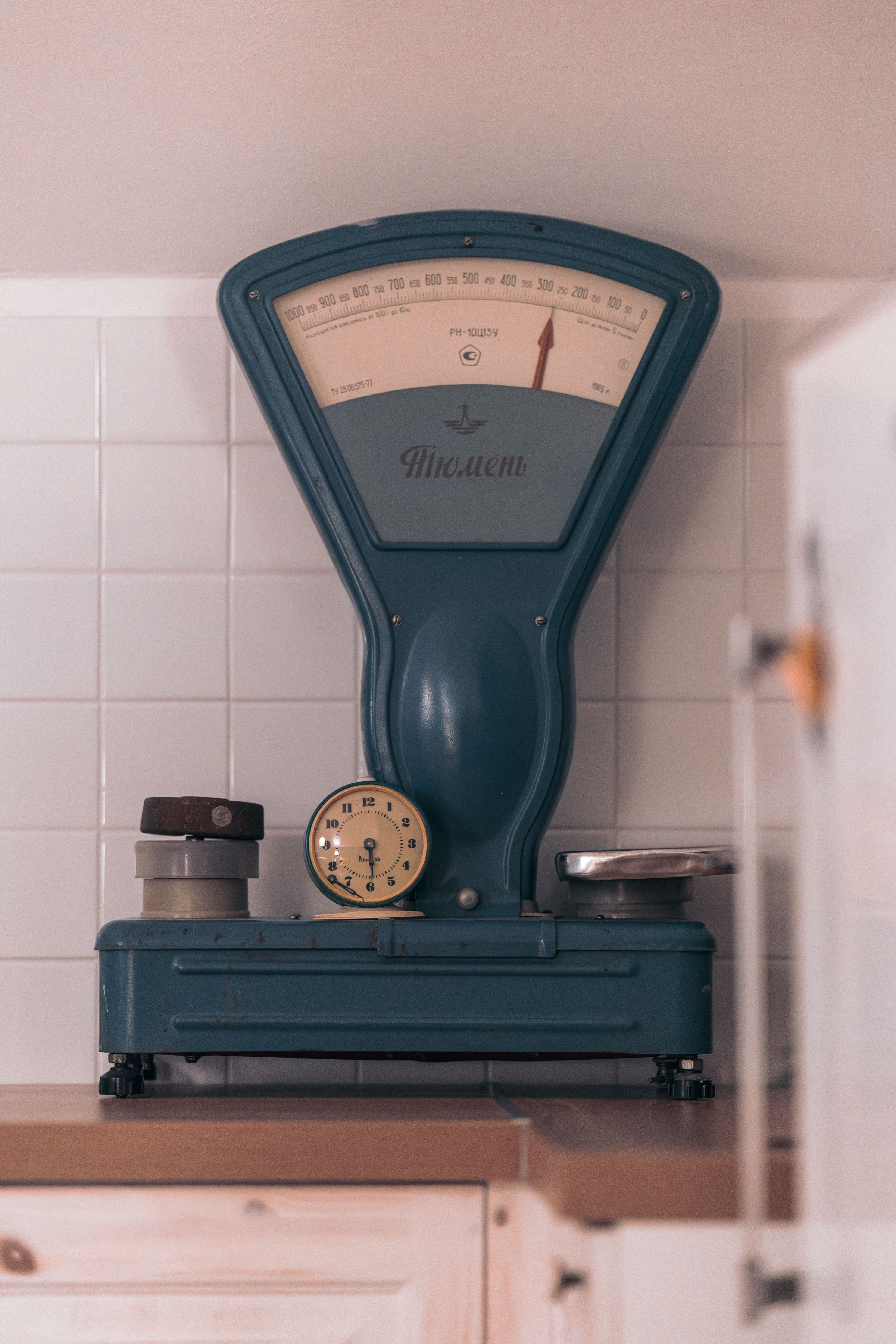 Fotomural Una báscula clásica de estilo vintage con un reloj mecánico al lado, colocada sobre una encimera de cocina alicatada.