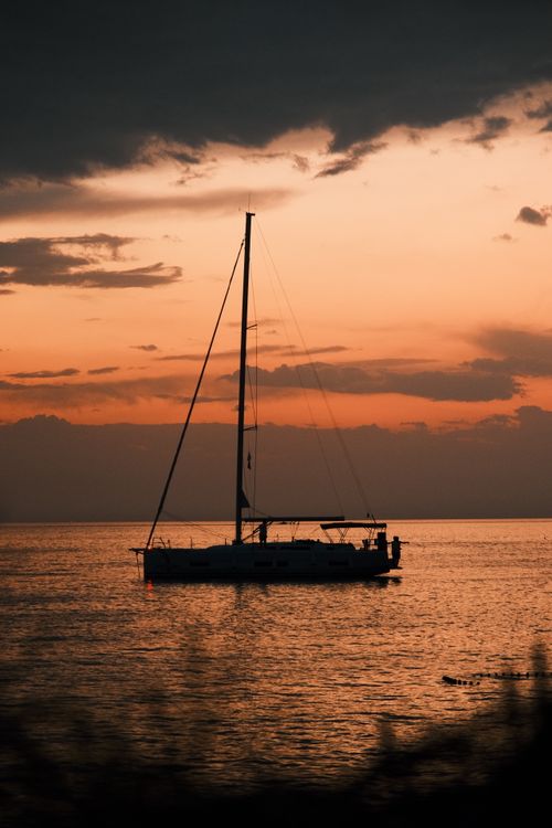 Free A peaceful yacht sails under a vivid sunset, casting reflections on a calm sea. Stock Photo
