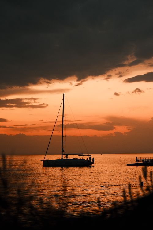 Free A peaceful sailboat silhouetted against a stunning orange sunset on a tranquil sea. Stock Photo