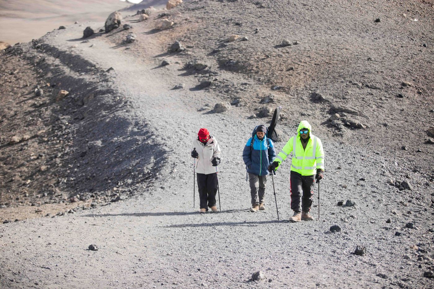 Three trekkers with poles and packs crossing the rocky volcanic terrain high on Kilimanjaro