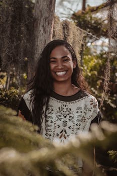 一位长发女子微笑着，在郁郁葱葱的森林中享受着阳光明媚的一天