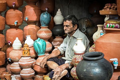 Free An elderly potter surrounded by traditional Indian clay pots in a vibrant market setting. Stock Photo
