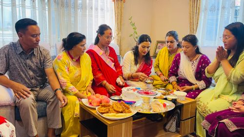 Free A family gathers indoors for a traditional Nepali celebration with food and ritual offerings. Stock Photo