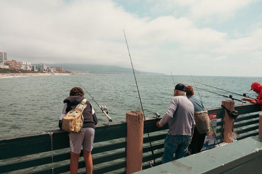 A group of people fishing on a pier in Los Angeles with ocean view.