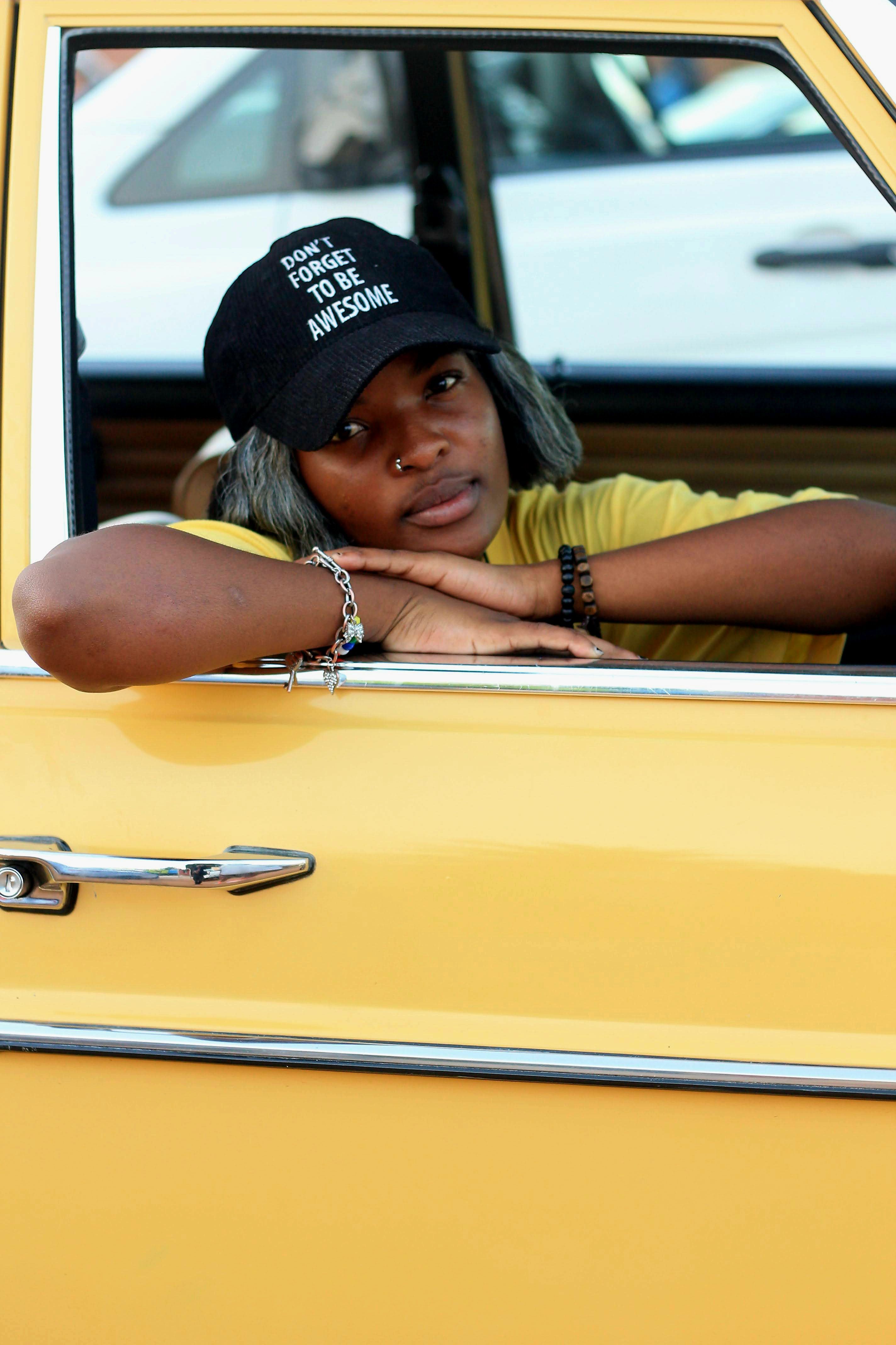 Portrait of a woman in a yellow car wearing a cap with an inspiring message in Soweto, South Africa.