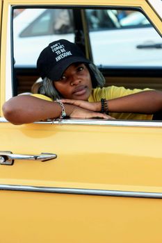 Portrait of a woman in a yellow car wearing a cap with an inspiring message in Soweto, South Africa.