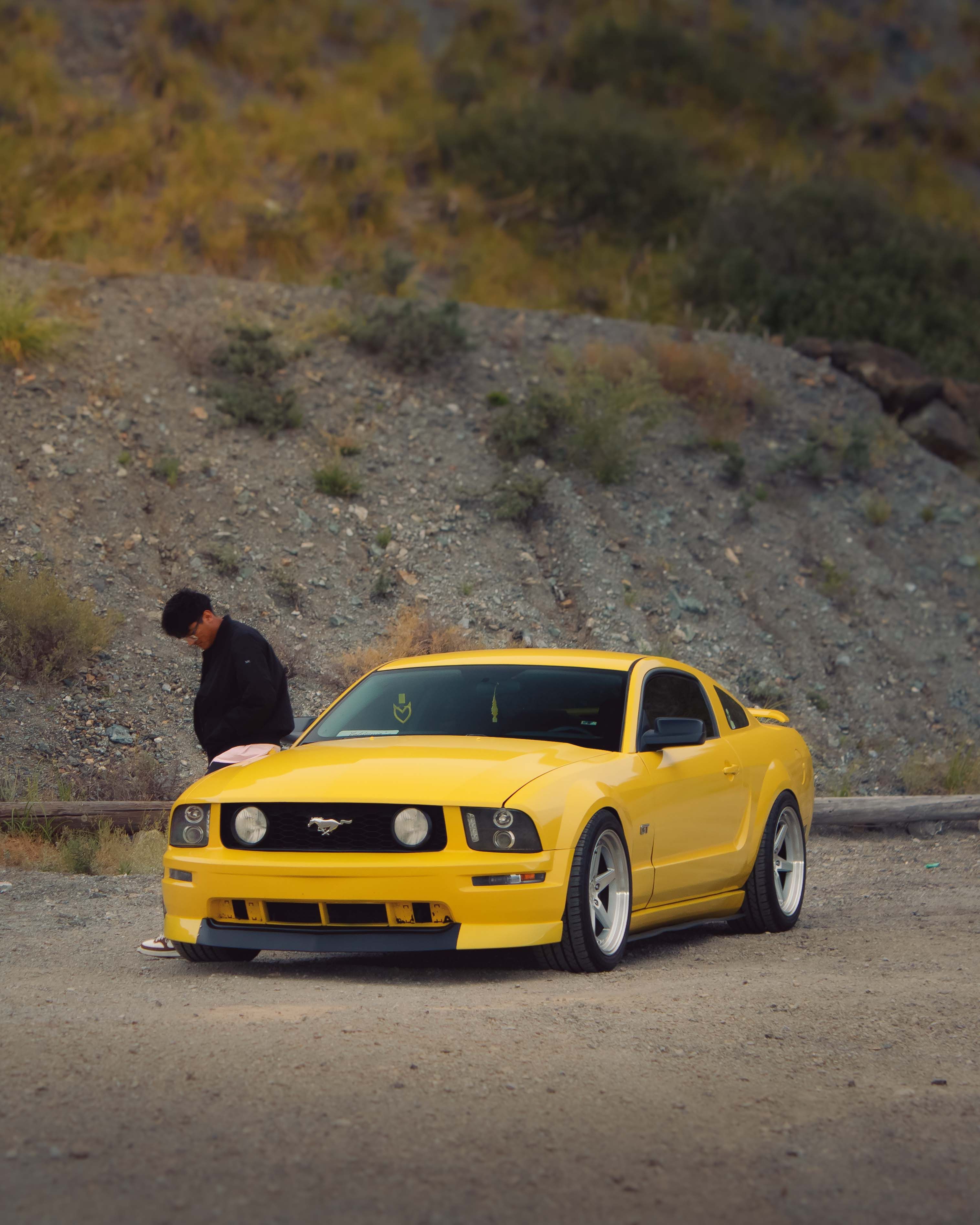A vibrant yellow sports car parked on a rocky roadside with a person nearby.