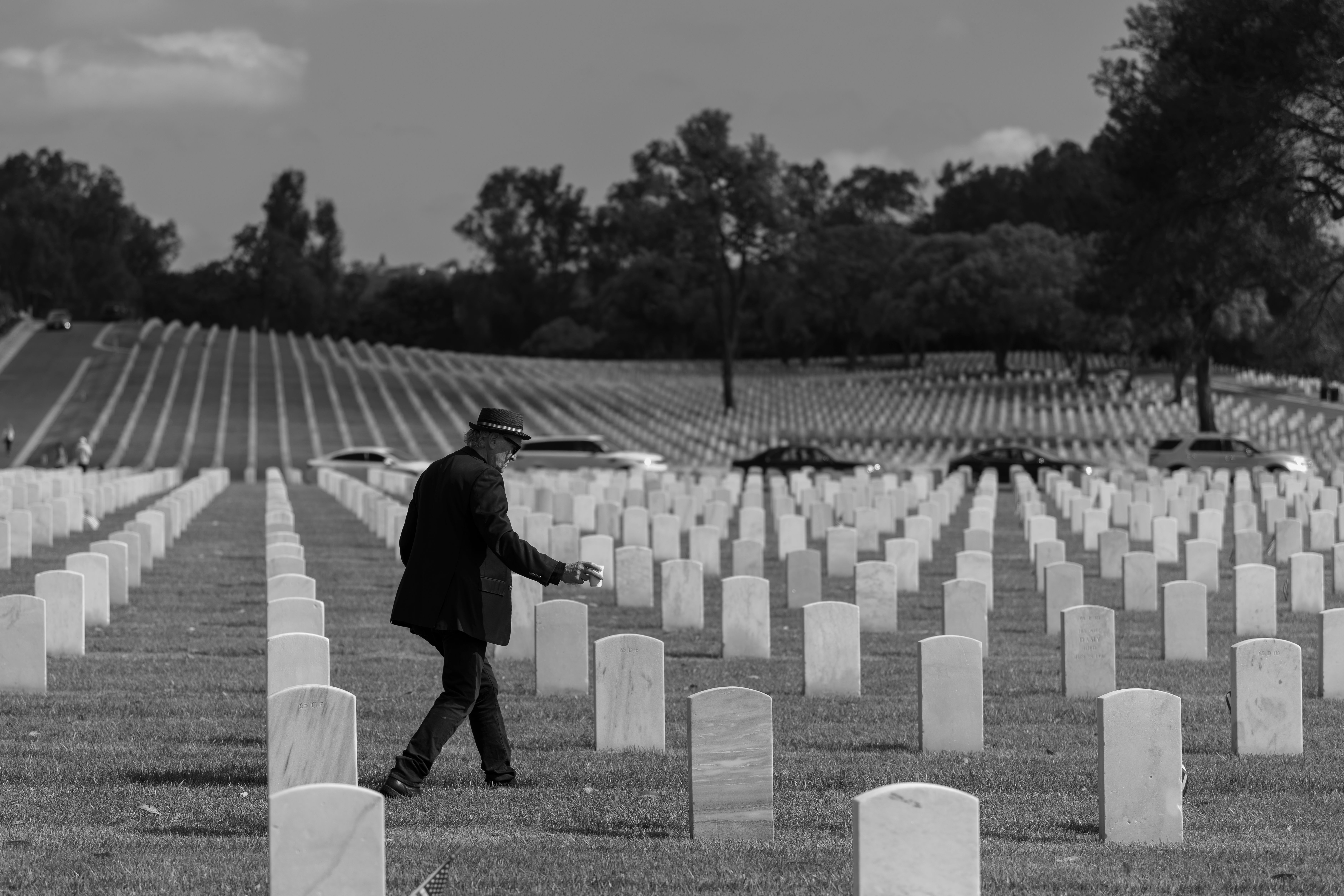 A man walks through a cemetery in Los Angeles, California, amidst rows of headstones, capturing a reflective moment.