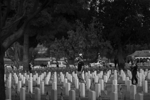 Black and white scene of people visiting a war memorial, displaying tributes and remembrance.