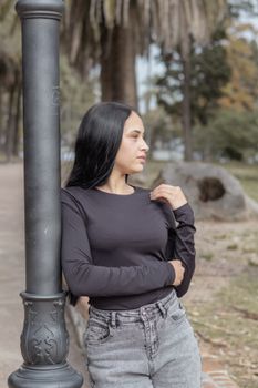 Profile of a young woman in a park in Montevideo during the day, leaning on a lamp post.