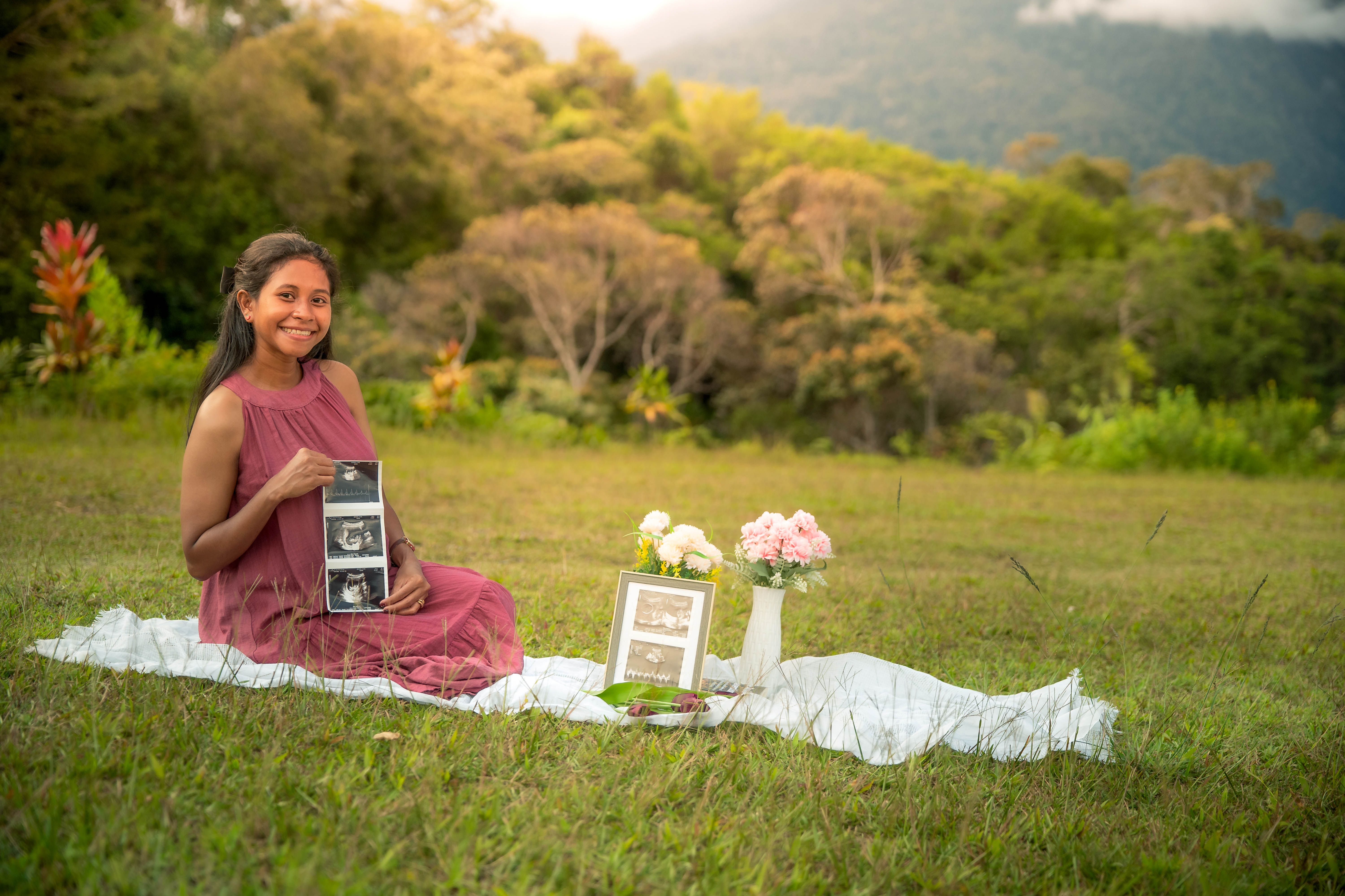 Pregnant woman showcasing sonogram on a picnic in a serene outdoor setting.