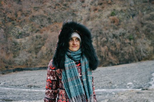 Woman in winter attire standing against a rocky mountain background.