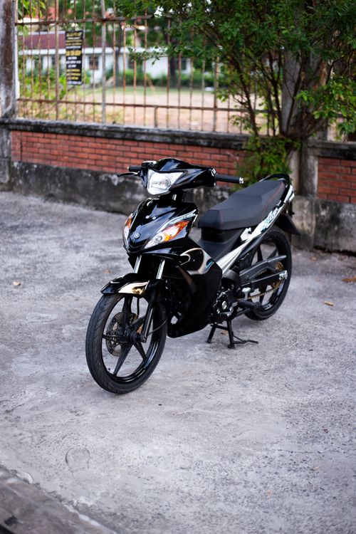 Free A sleek black motorbike parked outdoors on a concrete surface near a brick wall and green foliage. Stock Photo