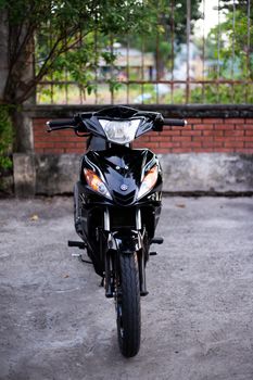 Front view of a black motorcycle parked outdoors against a brick wall.