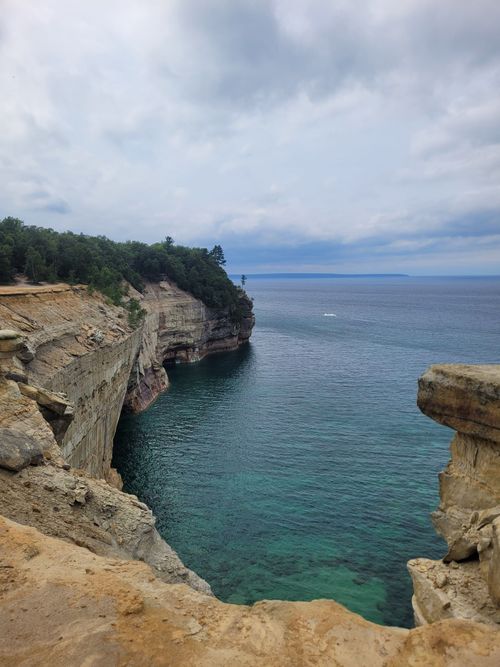 Free Dramatic cliffs extend into crystal clear lake waters under a cloudy sky, offering a breathtaking natural view. Stock Photo