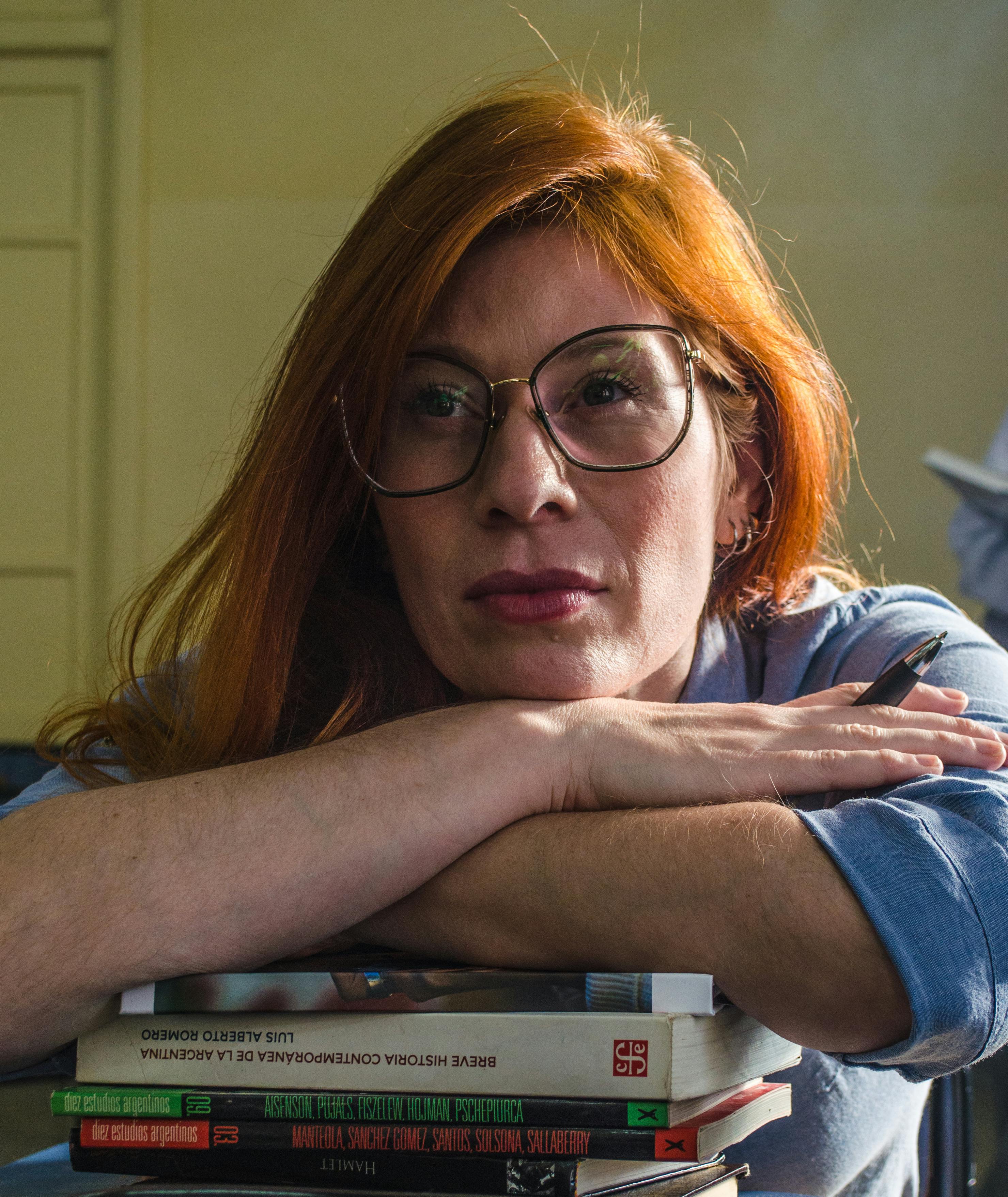 Portrait of a reflective woman leaning on a stack of books, indoors with natural light.