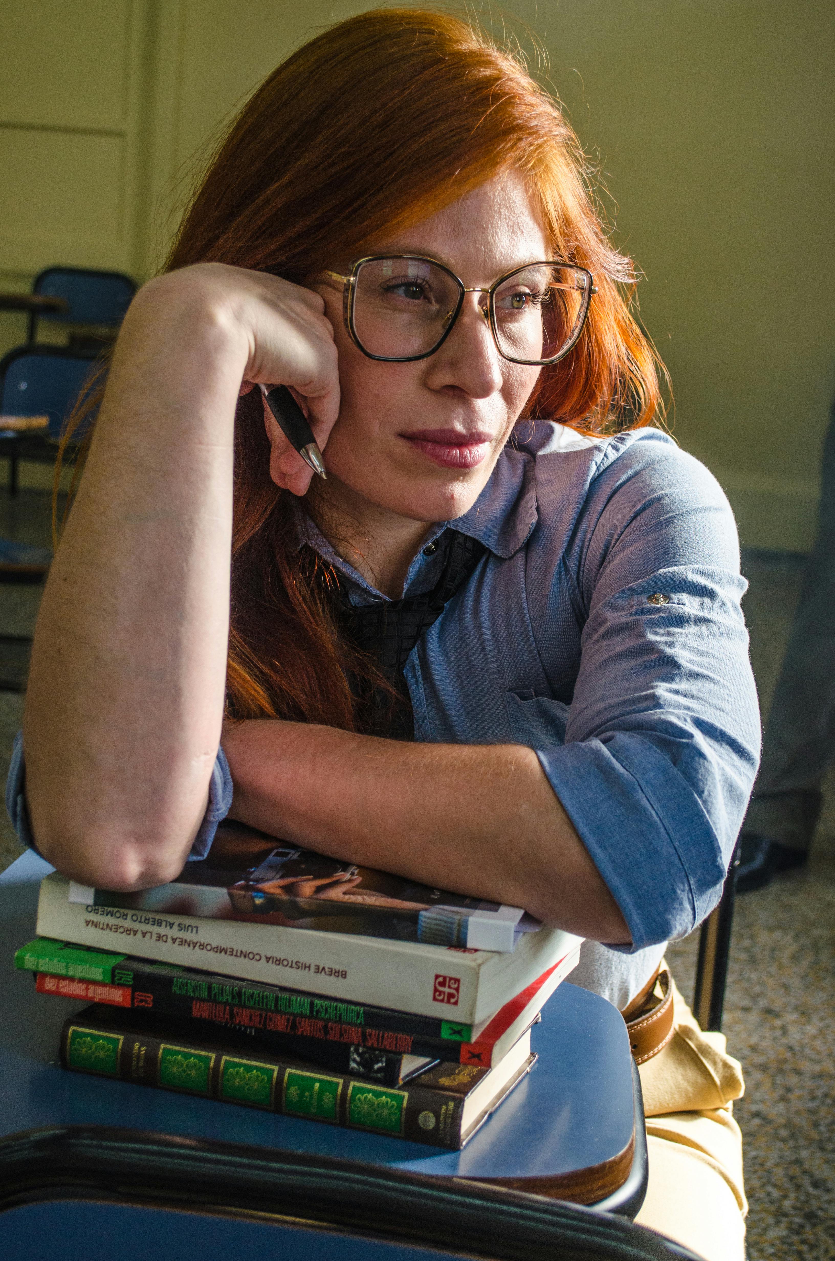 A person ponders in a Buenos Aires classroom, resting on books and a desk.