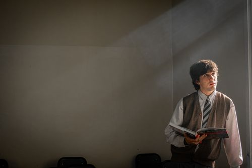 Free A man stands in a sunlit room, absorbed in a book. Light streams through a window. Stock Photo