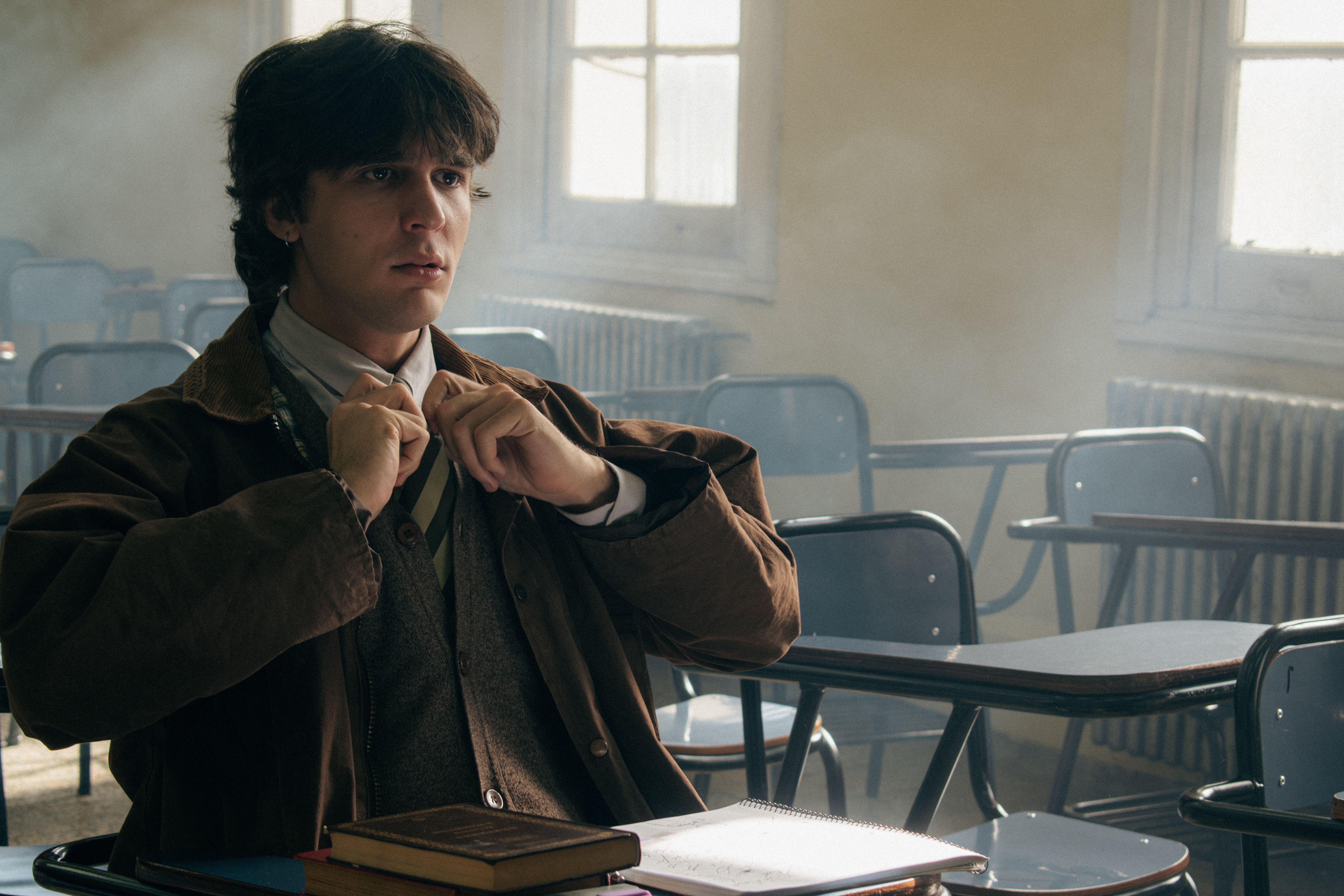 A student in a foggy, empty classroom adjusts his tie, reflecting a thoughtful mood.