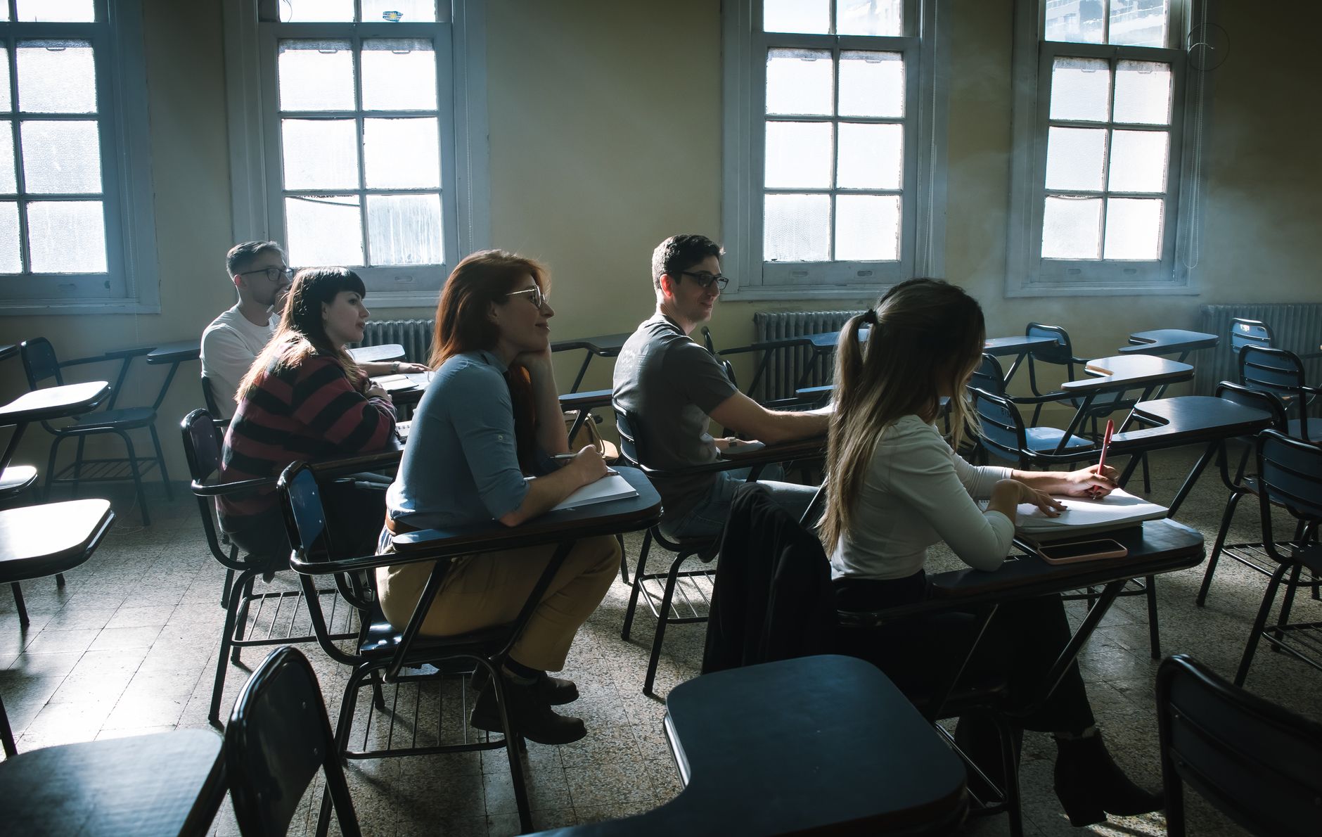 A diverse group of students attentively participating in a classroom lecture by window light.