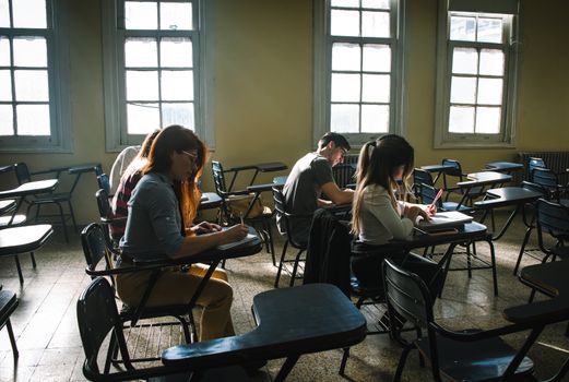 Students focused on writing during an exam in a sunlit classroom.