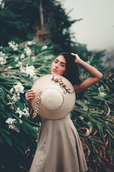 这是一幅年轻女子的肖像，她身着连衣裙，头戴装饰帽，四周环绕着郁郁葱葱的绿植与白花